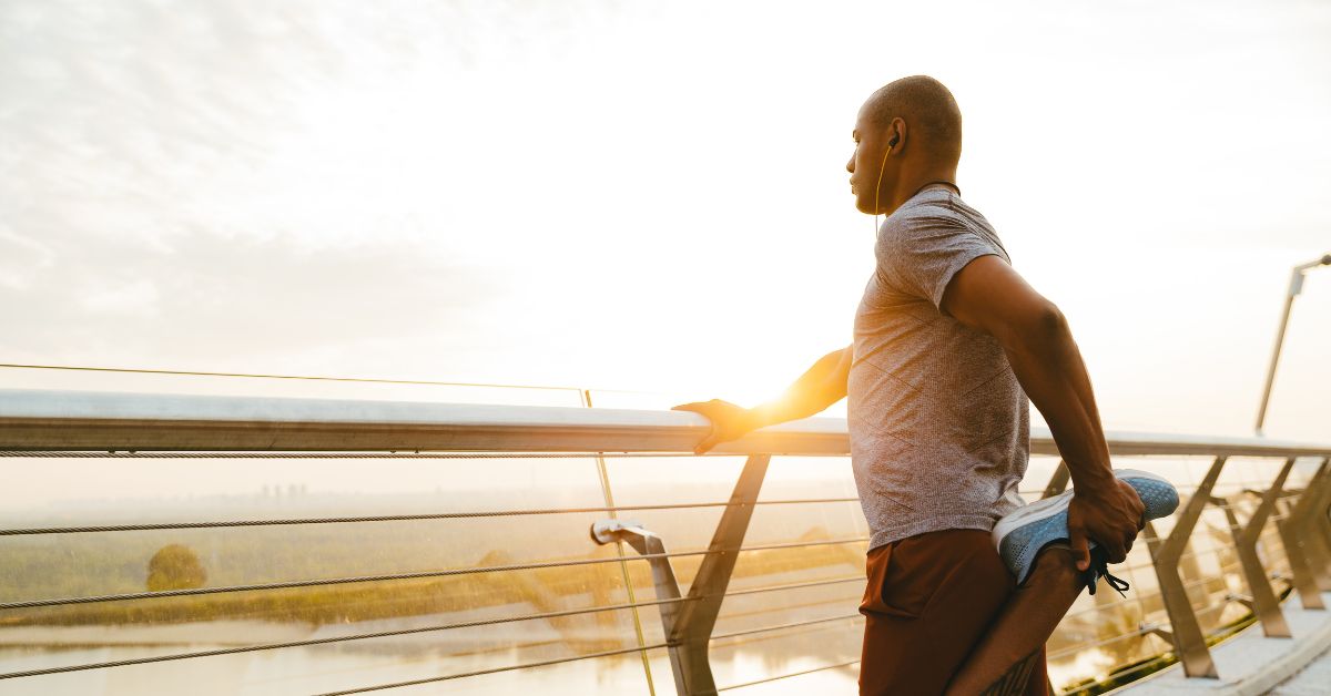 a person holding onto a railing and stretching their leg while looking out at the sunrise over a lake