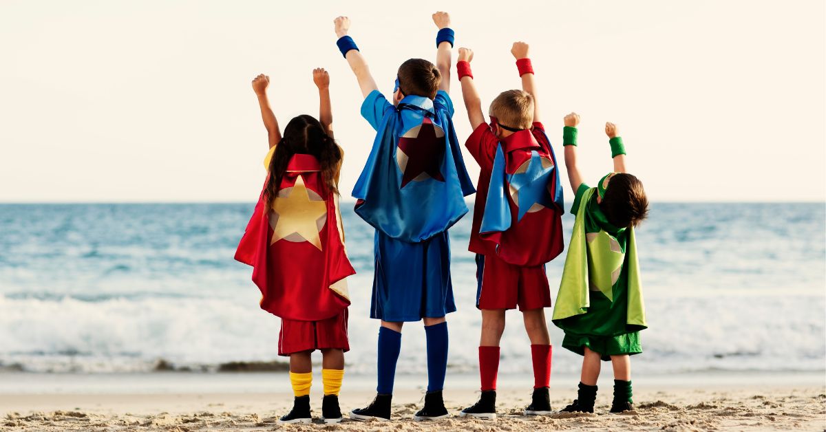 Image: 4 children standing on beach wearing super hero costumes