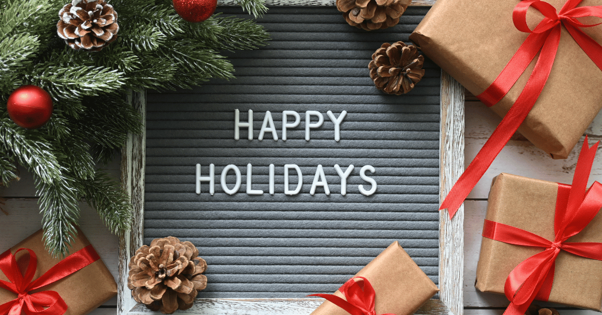 A holiday wreath, acorns, and brown gift boxes with red bows. The words "Happy Holidays" written in the middle