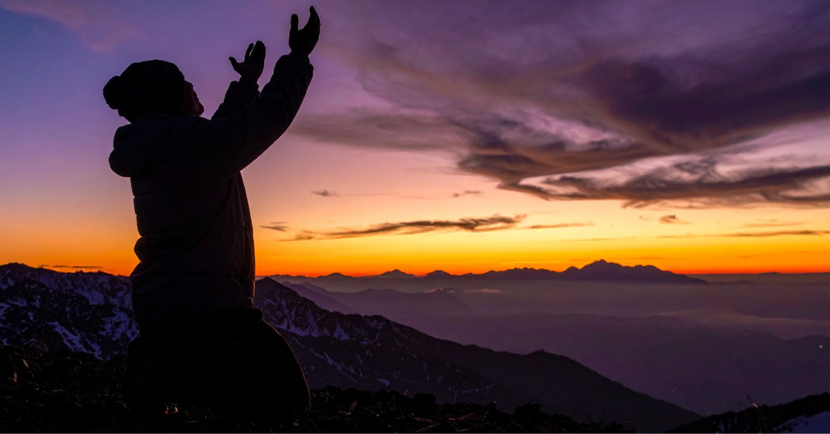 a person reaching their arms up looking out at a sunrise