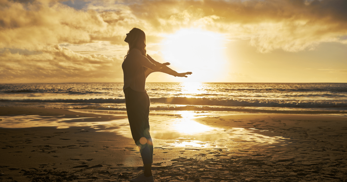 A person at the beach embracing the sunsetting over the ocean