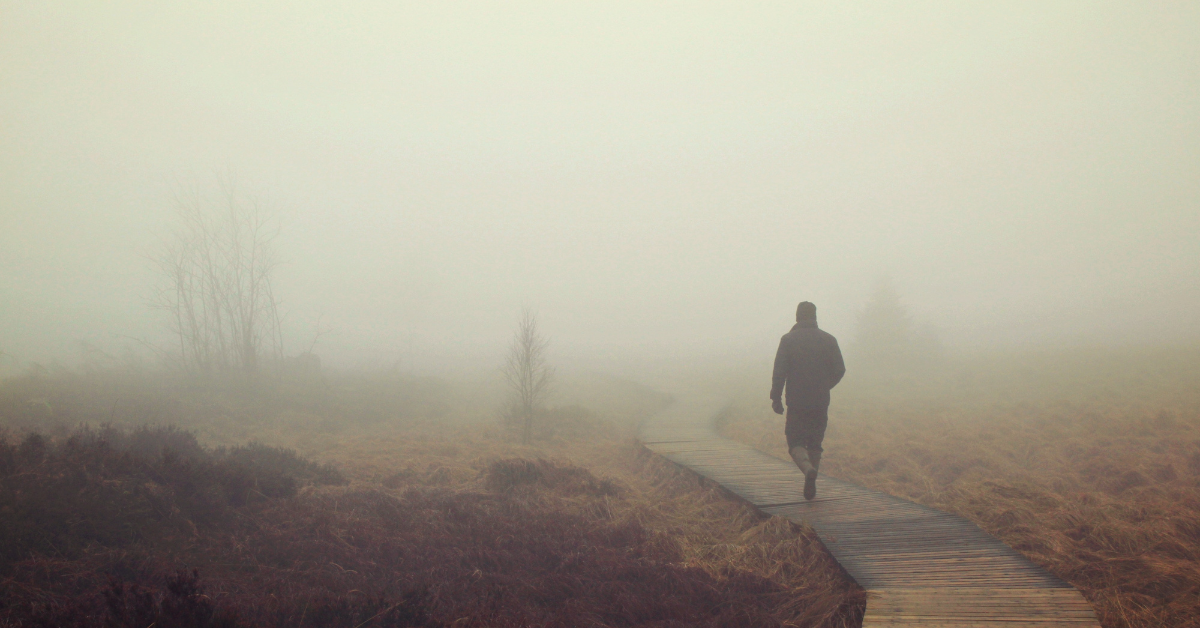 An individual walking on a wooden walkway in a foggy outdoor area