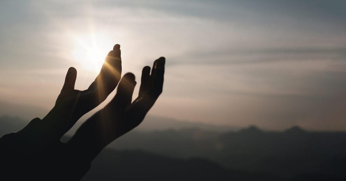 Two hands open and outstretched in front of a bleak sky