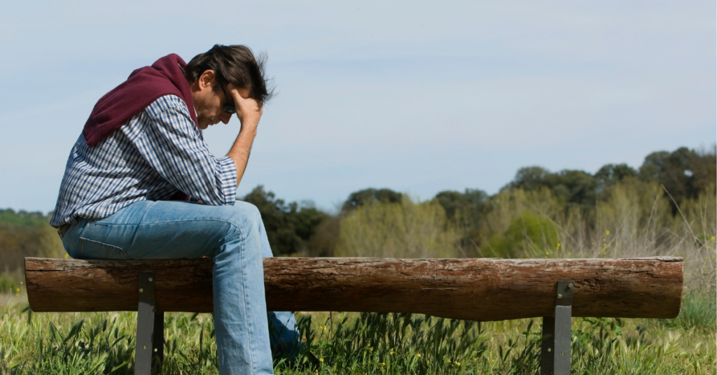 Man sitting on edge of bench, holding his head in his hands