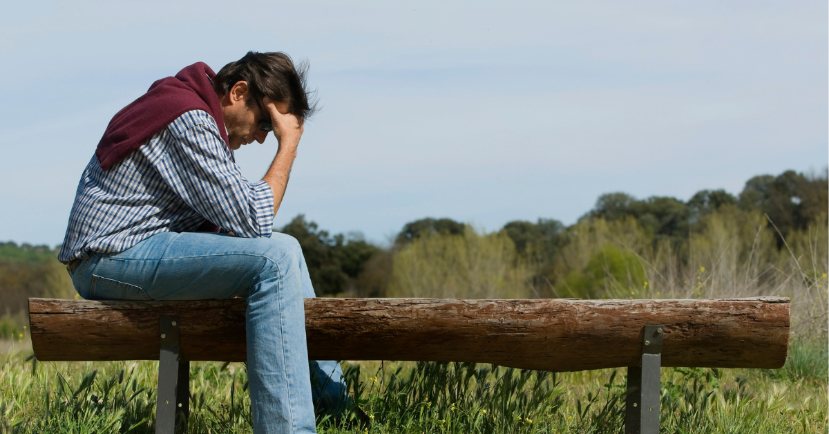 Man sitting on edge of bench, holding his head in his hands
