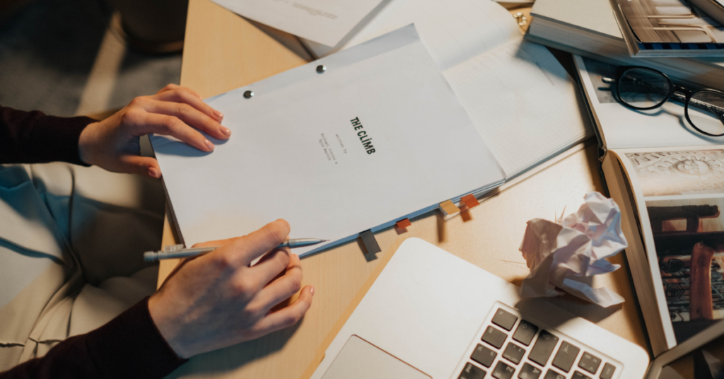 An individual holding a written report next to a laptop