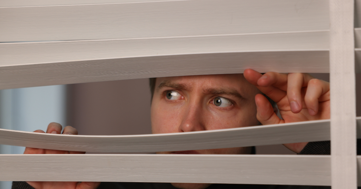 An individual looking through window blinds