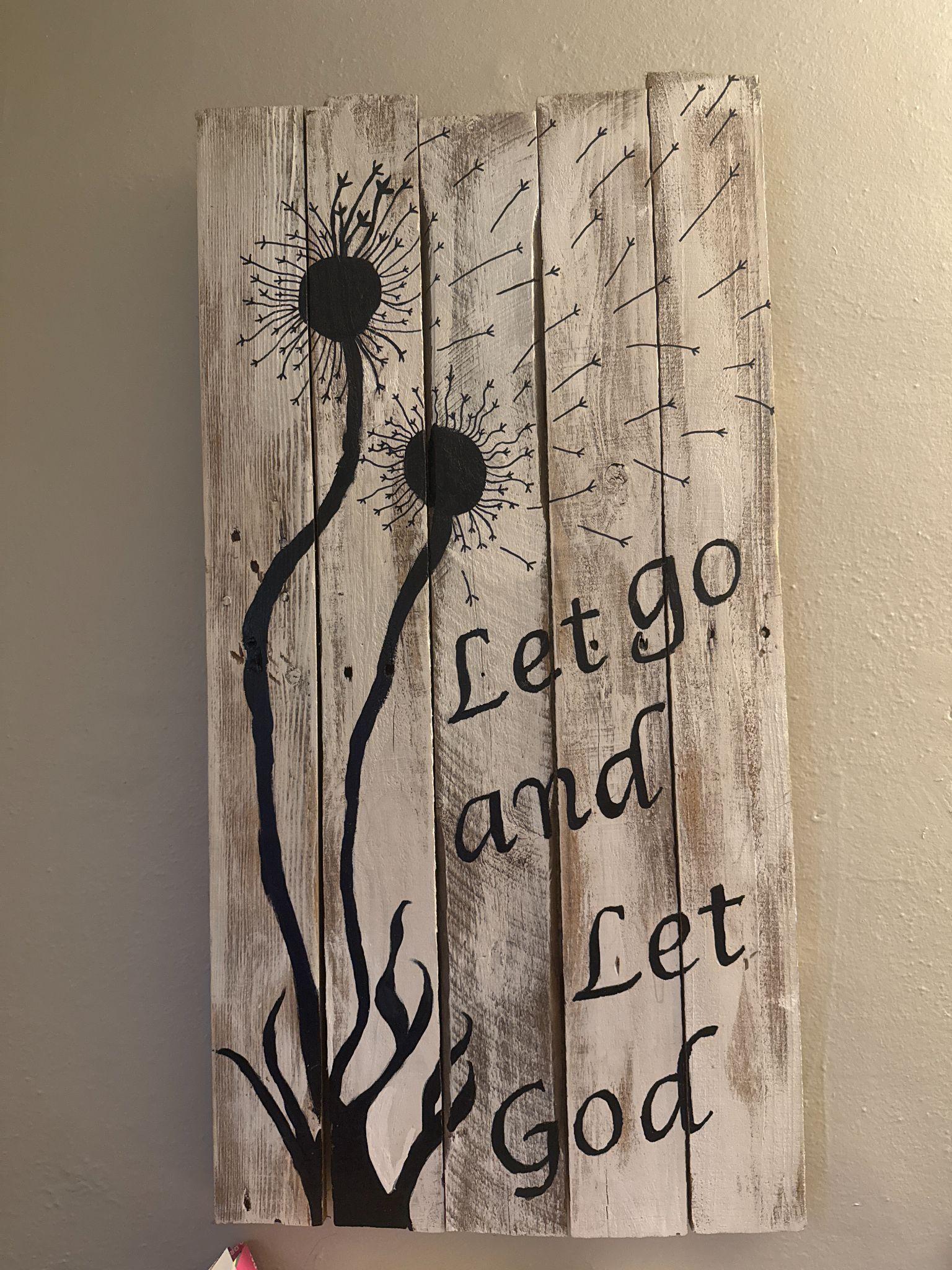 Hand-painted sign on weathered white pallet boards with black dandelion seed heads and the words Let go and Let God